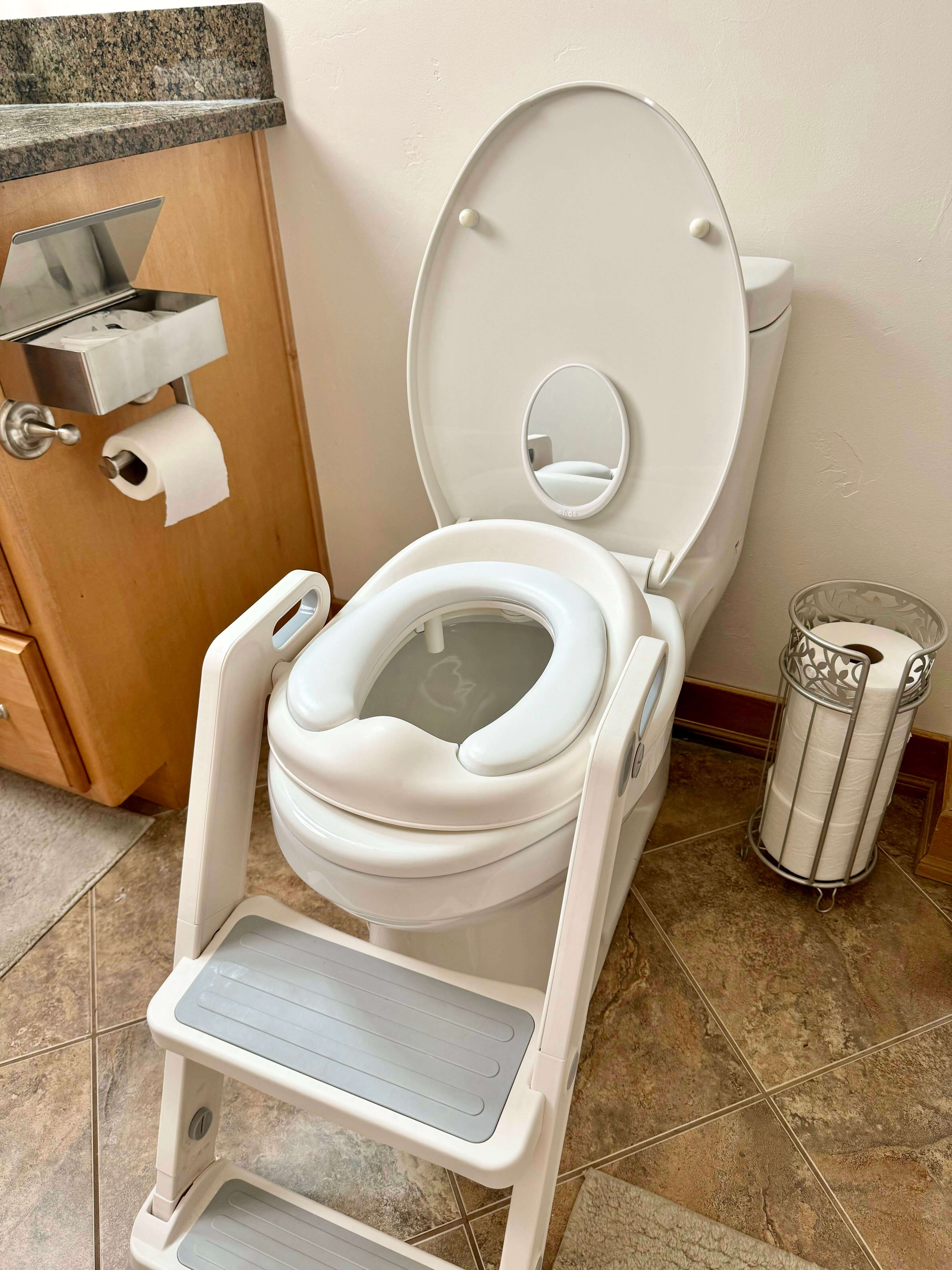 Toilet with an attached mirror on the lid, featuring a potty training seat and step stool for child bathroom independence